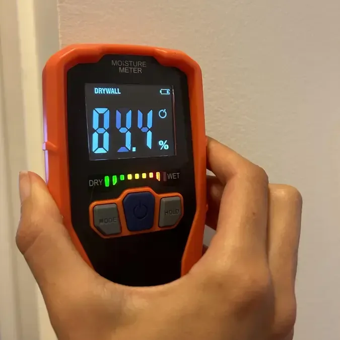 A pinless moisture meter taking a reading on a painted wall during structural drying